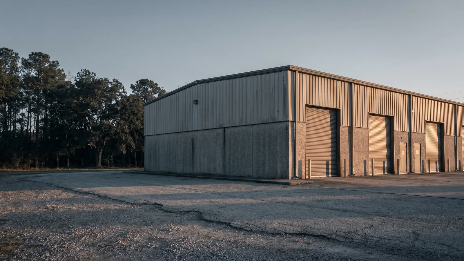Small-bay warehouse with a row of steel roll-up doors in soft golden-hour morning light